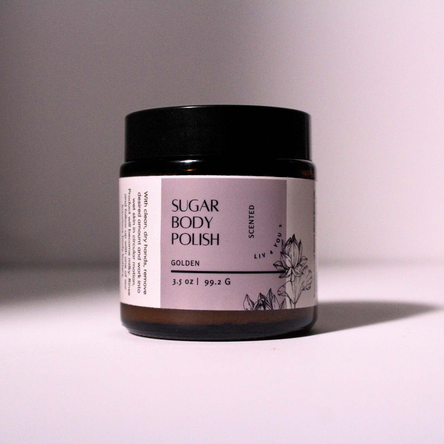 Sugar Body Polish in brown glass jar with black lid, white and purple label with black font.