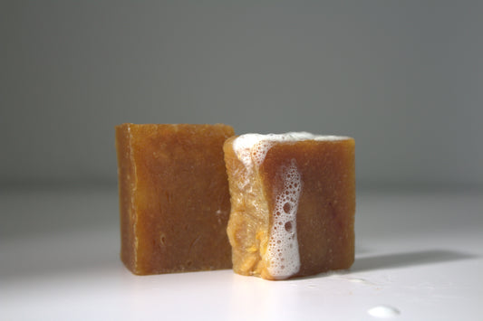 Saffron honey turmeric face soap on white foundation, gray background, and white suds on right side soap